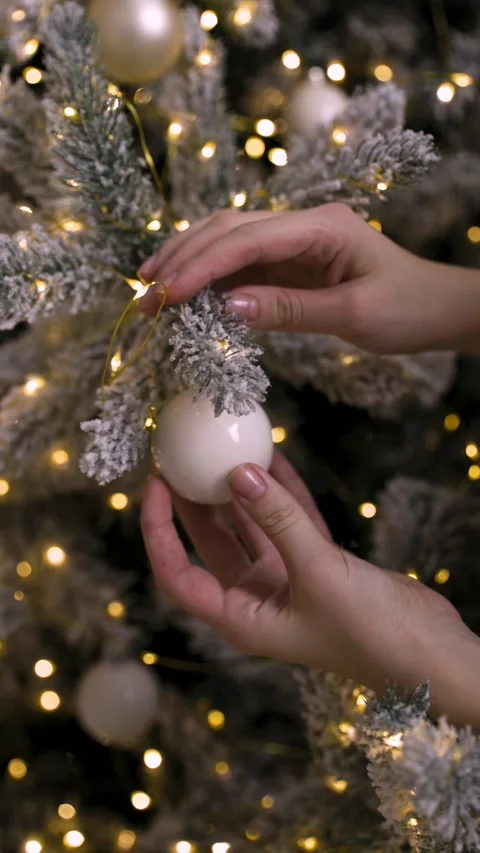 Two hands carefully place a white ornament on a snowy Christmas tree Stock Footage 323224129
