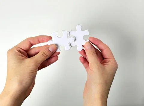 Two hands connect white puzzle pieces against a clean background, symbolizing Stock Photos