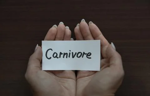 Two hands cupped together holding a white card with "Carnivore" handwritten.. Stock Photos