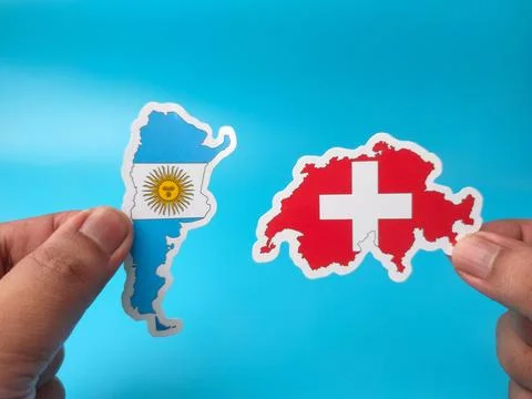 Two hands display paper cutouts of the country shapes of Argentina and Swit.. Stock Photos