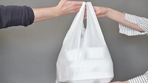 Two hands exchange a white plastic bag containing items against a neutral Vidéo 337556885