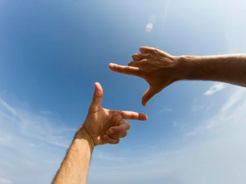 Two hands form a frame in front of a blue sky Stock Photos