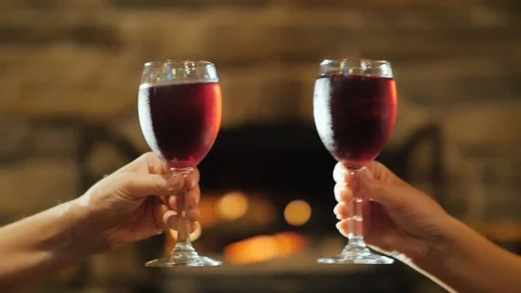 Two hands with glasses of red wine. Clinking against the background of a burning Stock Footage 94059520