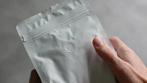 Two hands hold and squeeze a light gray coffee pouch, showing the round aroma Stock Footage 347632745