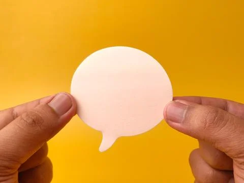 Two hands hold a blank white speech bubble cutout horizontally against a br.. Stock Photos
