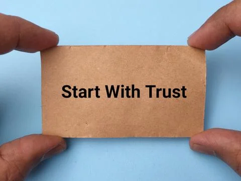 Two hands hold a brown paper card reading Start With Trust against a light .. Fotos de archivo