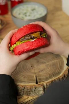 Two hands hold a burger with a red bun that has lettuce and cheese Stockfoto's