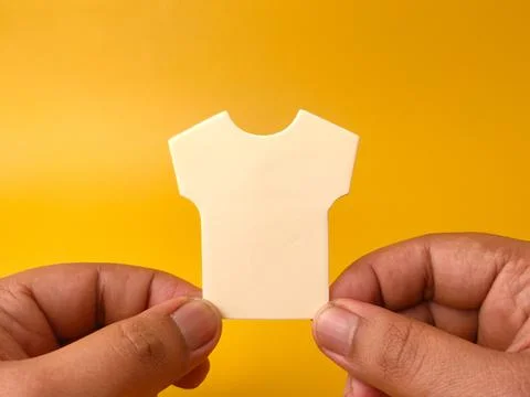 Two hands hold an empty white shirt-shaped paper cutout flat against a soli.. 库存照片