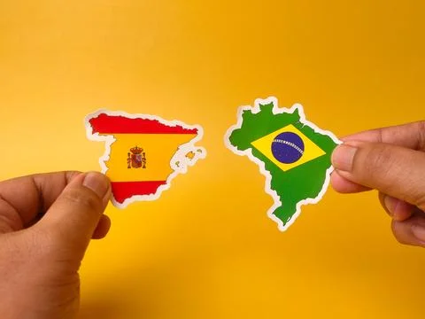 Two hands hold flag-colored map cutouts of Spain and Brazil opposite each o.. Stock Photos