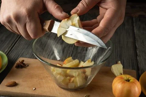 Two hands hold a knife, slicing apples into pieces over a clear bowl. The w.. Stock Photos