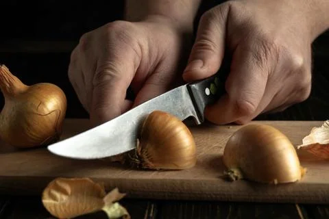 Two hands hold a knife while cutting onions on a wooden board. The setting sh Stock Photos