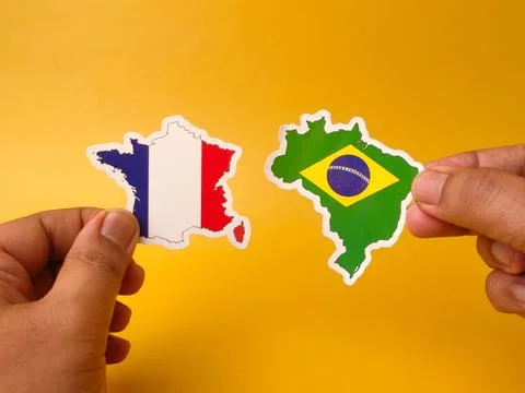 Two hands hold paper cutouts of France and Brazil map shapes with their res.. Stock Photos