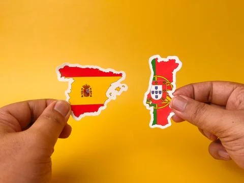 Two hands hold paper map cutouts of Spain and Portugal decorated with their.. Stock Photos