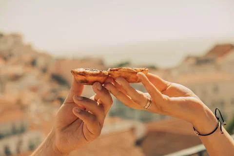 Two hands hold pastry while showing city in background during daylight hours  库存照片
