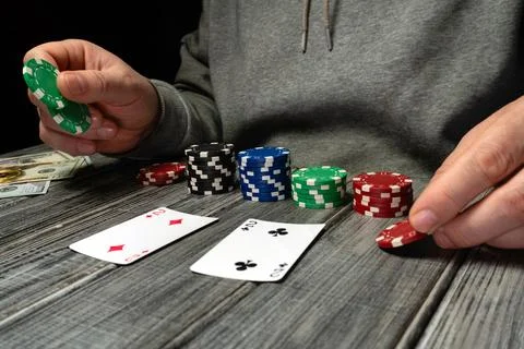 Two hands hold poker chips and cards on a wooden table at night. There are .. Stock Photos