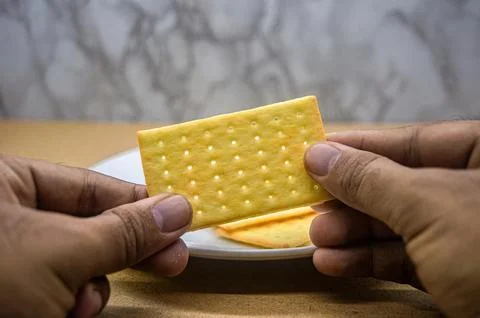 Two hands hold a single golden, rectangular cracker, ready to be eaten. A p.. Foto stock