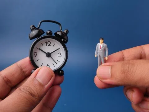 Two hands hold a small black alarm clock face-to-face with a miniature busi.. Stock Photos