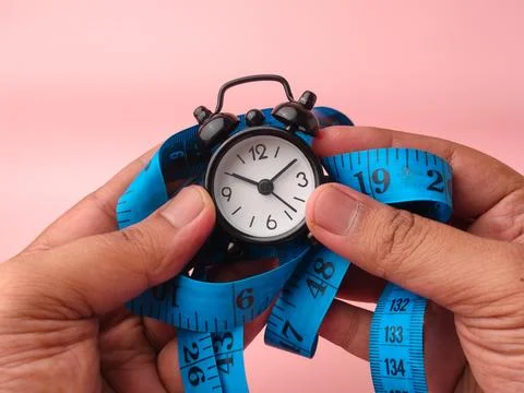 Two hands hold a small black mechanical alarm clock wrapped in a coiled blu.. Stock Photos