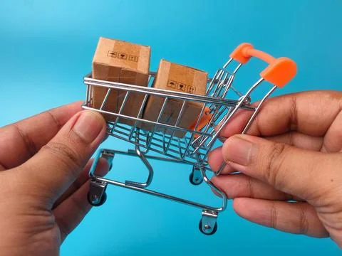 Two hands hold a small metal shopping cart containing two miniature brown c.. Stock Photos
