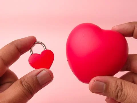 Two hands hold a small red heart-shaped padlock next to a larger red stress.. Stock Photos