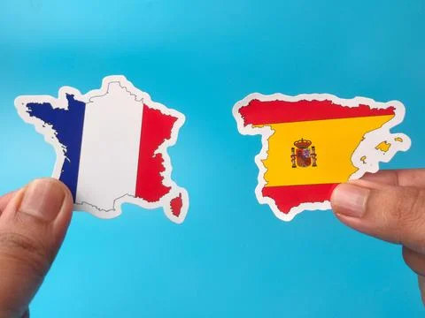 Two hands hold up stickers shaped like the country maps of France and Spain.. Stock Photos
