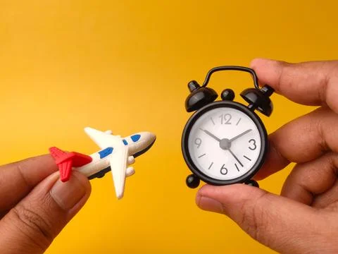 Two hands hold a tiny white toy airplane and a small black alarm clock over.. Stock Photos