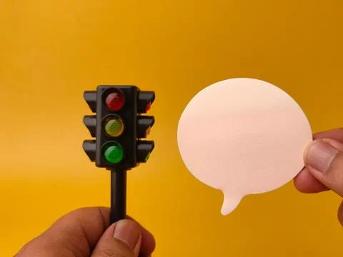 Two hands hold a toy vertical traffic light and a blank white paper speech .. Stock Photos