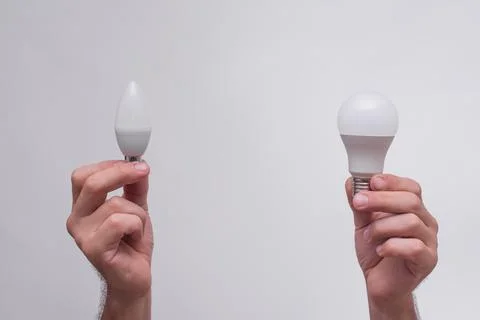 Two hands holding energy-efficient LED bulbs, one with a classic shape and .. Stock Photos
