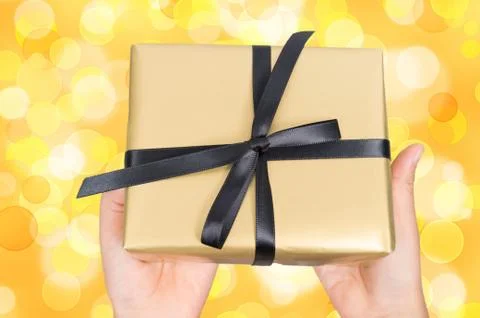 Two hands  holding a gift wrapped in golden paper Stock Photos