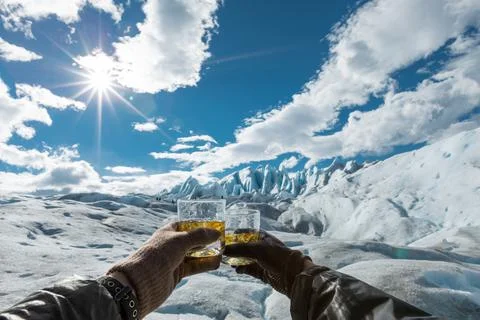 Two hands holding glasses with drinks in cheers gesture at Perito Moreno Glacier Stock Photos