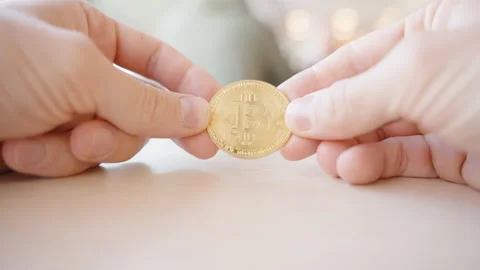Two Hands Holding a Golden Bitcoin Coin on a Wooden Surface with Soft Background Stock Footage 296533295