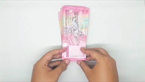 Two hands holding out stack of Indonesian banknotes in the 100,000 denomination Stock Footage 302318960