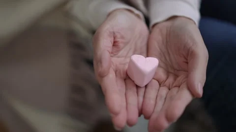 Two hands holding a pink marshmallow heart, symbolizing love and kindness Stock Footage 309381269