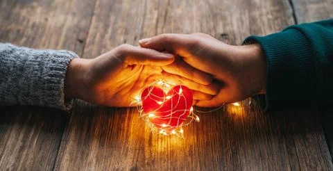 Two hands holding a red heart shape covered with led lights on wooden and bokeh Stock Photos