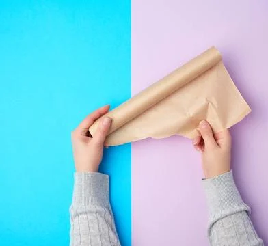 Two hands holding a roll of brown parchment paper on a colored background ... Stock Photos
