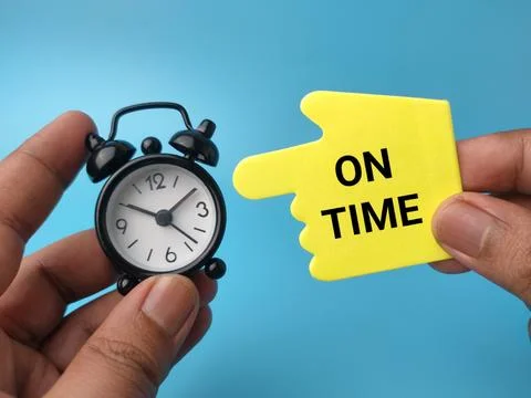 Two hands holding a small black alarm clock and a yellow hand-shaped pointe.. Stock Photos