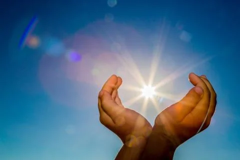 Two hands holding the sun on a blue sky background Stock Photos