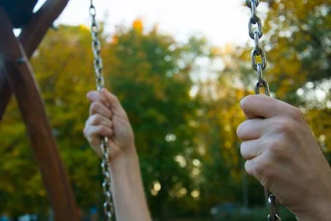 Two hands holding tight the chains of the child swing Stock Photos