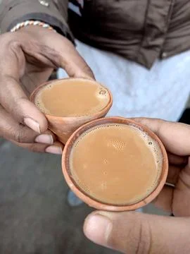 Two hands holding warm cups of chai in rustic clay kulhads Stock Photos