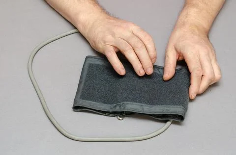 Two Hands of a middle-aged man holding the cuff of a digital blood pressure m Stock Photos