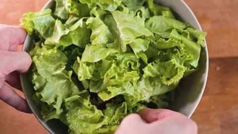 Two hands mix fresh greens in a large bowl on a wooden surface. The action Stock Footage 338290402