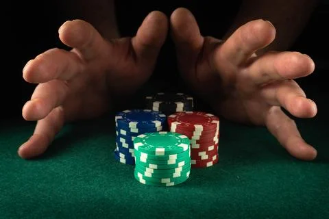 Two hands reach out over a stack of poker chips arranged on a green felt ta.. Foto stock
