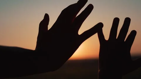 Two hands reach toward sunset creating silhouettes at horizon. People connect Stock Footage 342604498