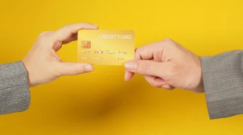 Two hands send and hold a gold credit card on yellow background. Arms wear a  Stock Photos