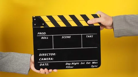 Two hands send and hold a Black clapper board on yellow background. Arms wear Stock Photos