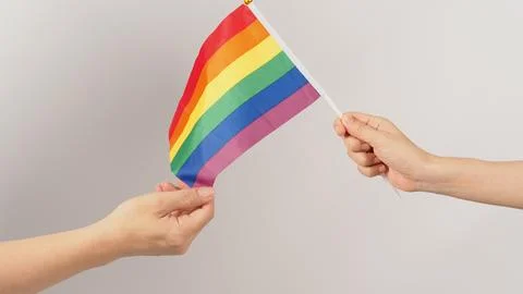 Two hands send and receive a rainbow flag on white background. LGBT CONCEPT.. Stock Photos