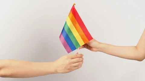 Two hands send and recive a rainbow flag on white background. LGBT CONCEPT. Stock Photos