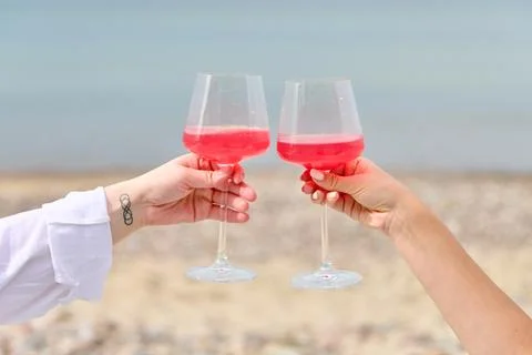 Two hands toasting pink wine glasses by sea during outdoor picnic Stock Photos