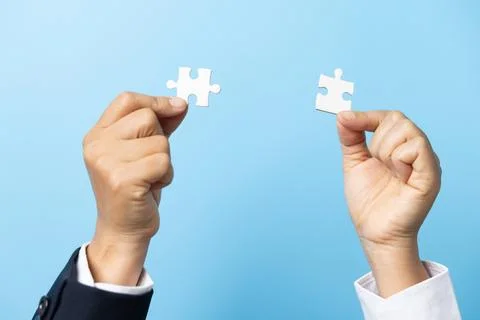 Two hands trying to connect couple puzzle piece on blue background. Teamwor.. Stock Photos