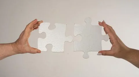 Two hands trying to connect puzzle piece on gray background. Teamwork conce.. Stock Photos